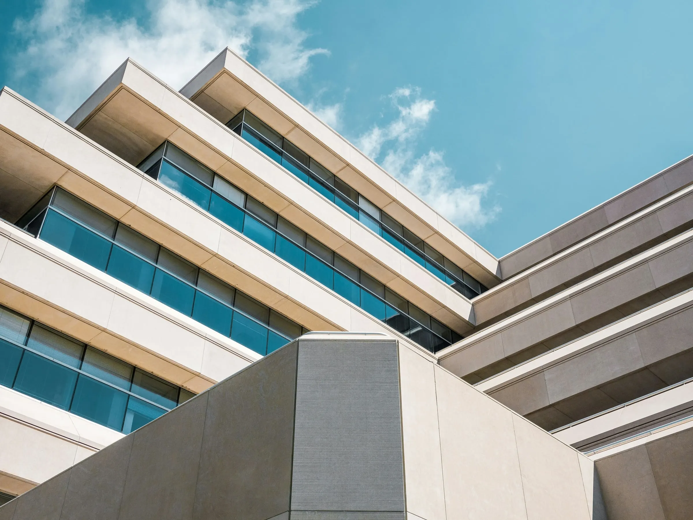Low-angle view of a modern office building with teal glass against a blue sky