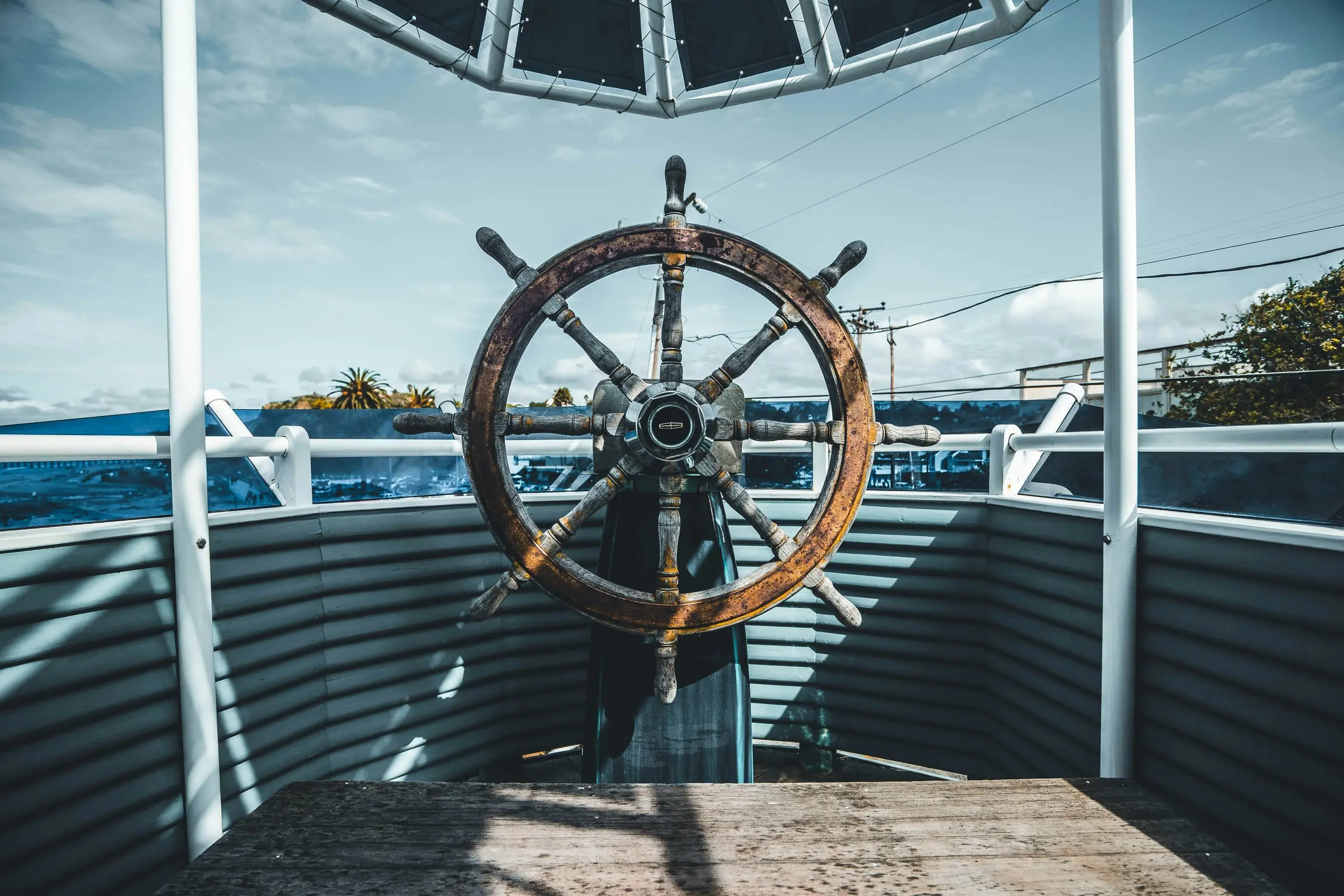 A wooden ship's wheel at the helm of a boat, looking out over open water